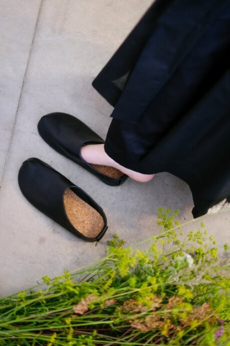 1. Woman wearing Kyoto black slippers by Omaking, sitting with a bouquet, showcasing minimalist design and comfort