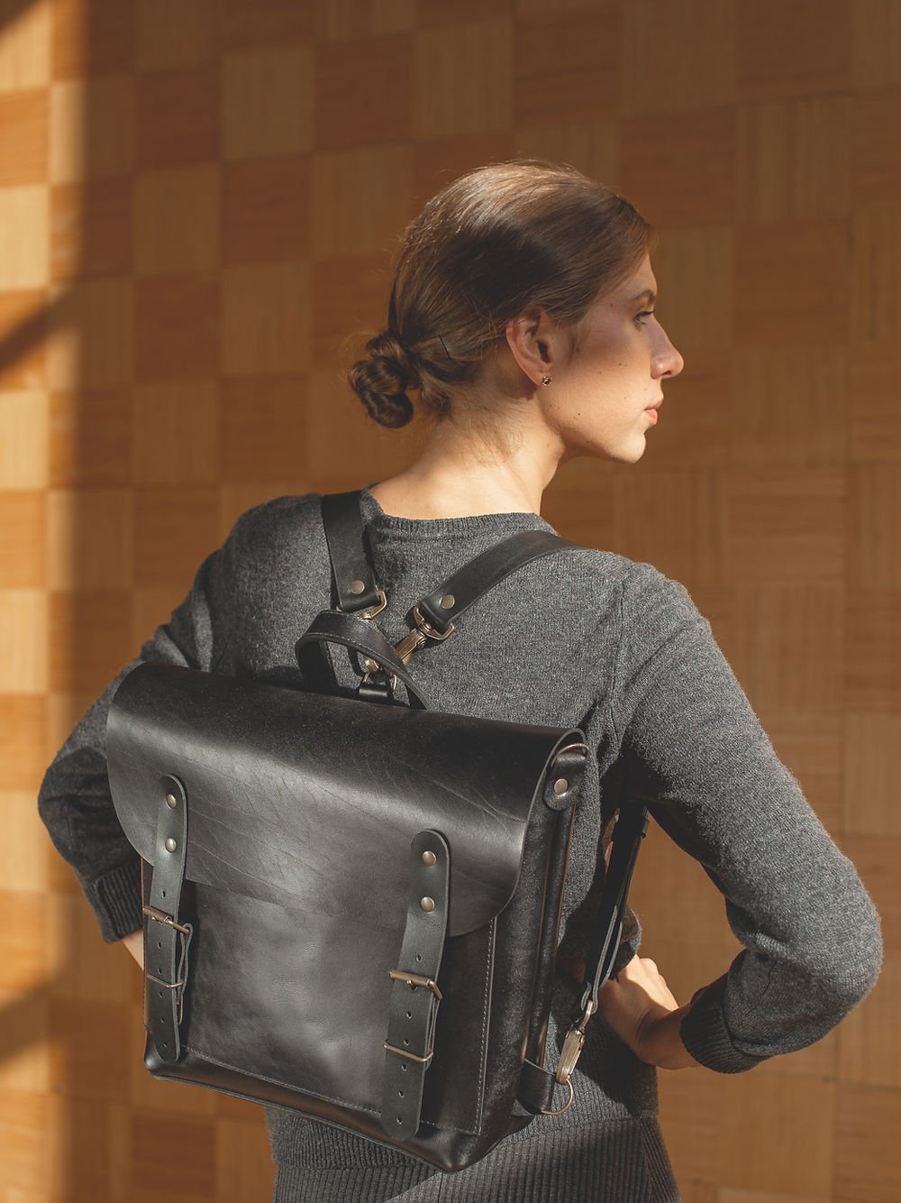 1. Woman wearing TOKS VISOKS BENJAMIN Backpack in black leather, shown from the side in a lifestyle setting