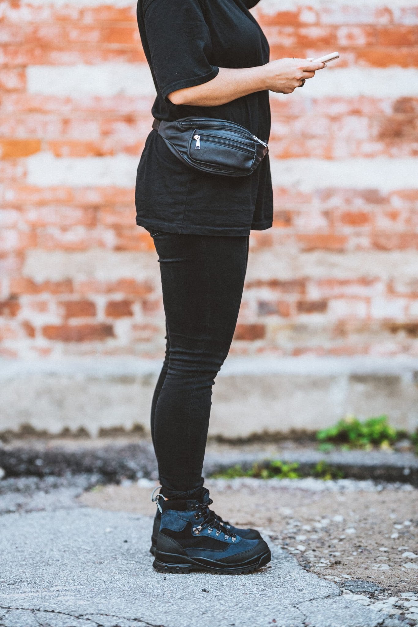 1. Woman wearing Papillon Leather Bum Bag No. 22 in black, styled with black outfit, shown in side view