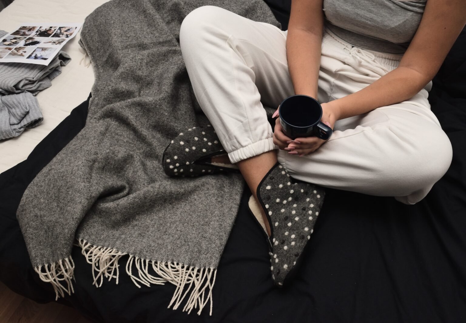 1. Woman wearing Omaking Barefoot Wool Slippers Trolla with dots, sitting on bed with blanket and holding a mug