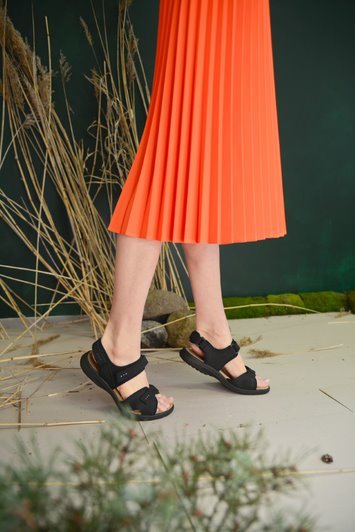 1. Women's black leather sandals by Omaking worn with an orange skirt in a lifestyle setting