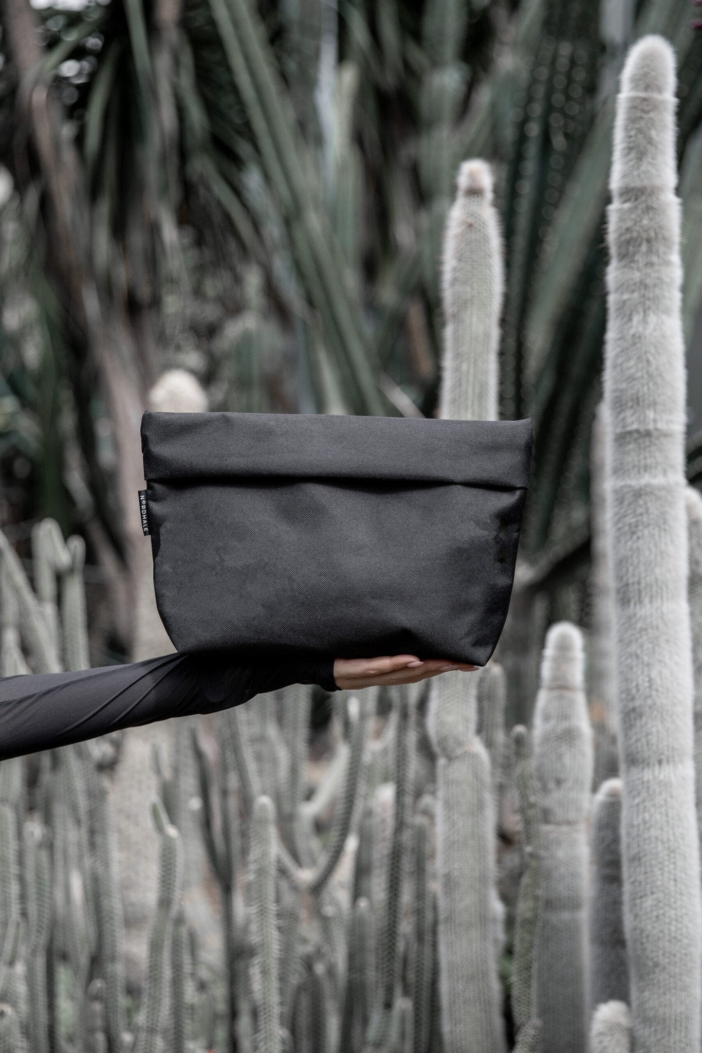 1. Nordhale NES Toiletry Bag in black held against a cactus background, showcasing minimalist design