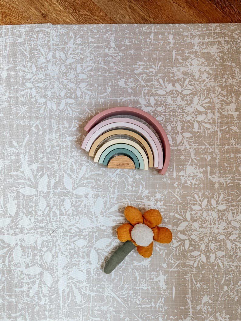 1. Vintage beige foam puzzle playmat with floral pattern, featuring a colorful wooden rainbow and plush flower toy on top