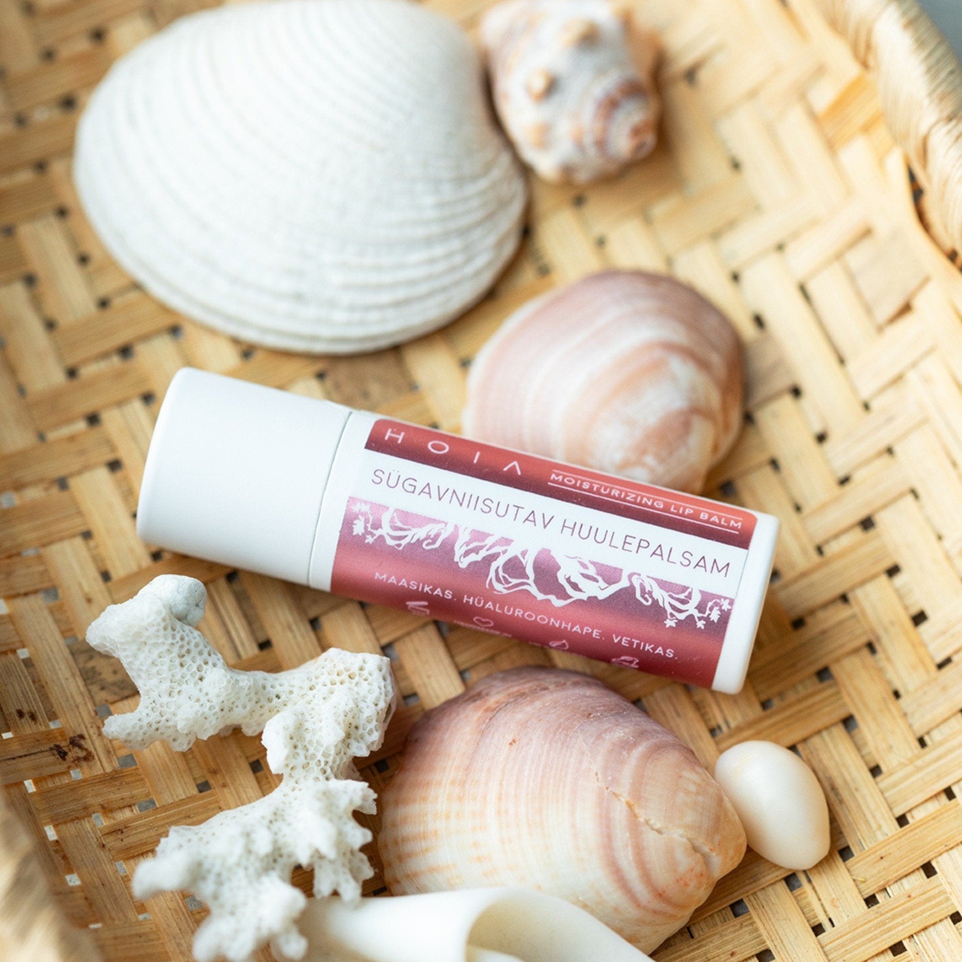 1. HOIA homespa deeply hydrating lip balm with monoi butter and strawberry seed oil, shown with seashells on a woven surface