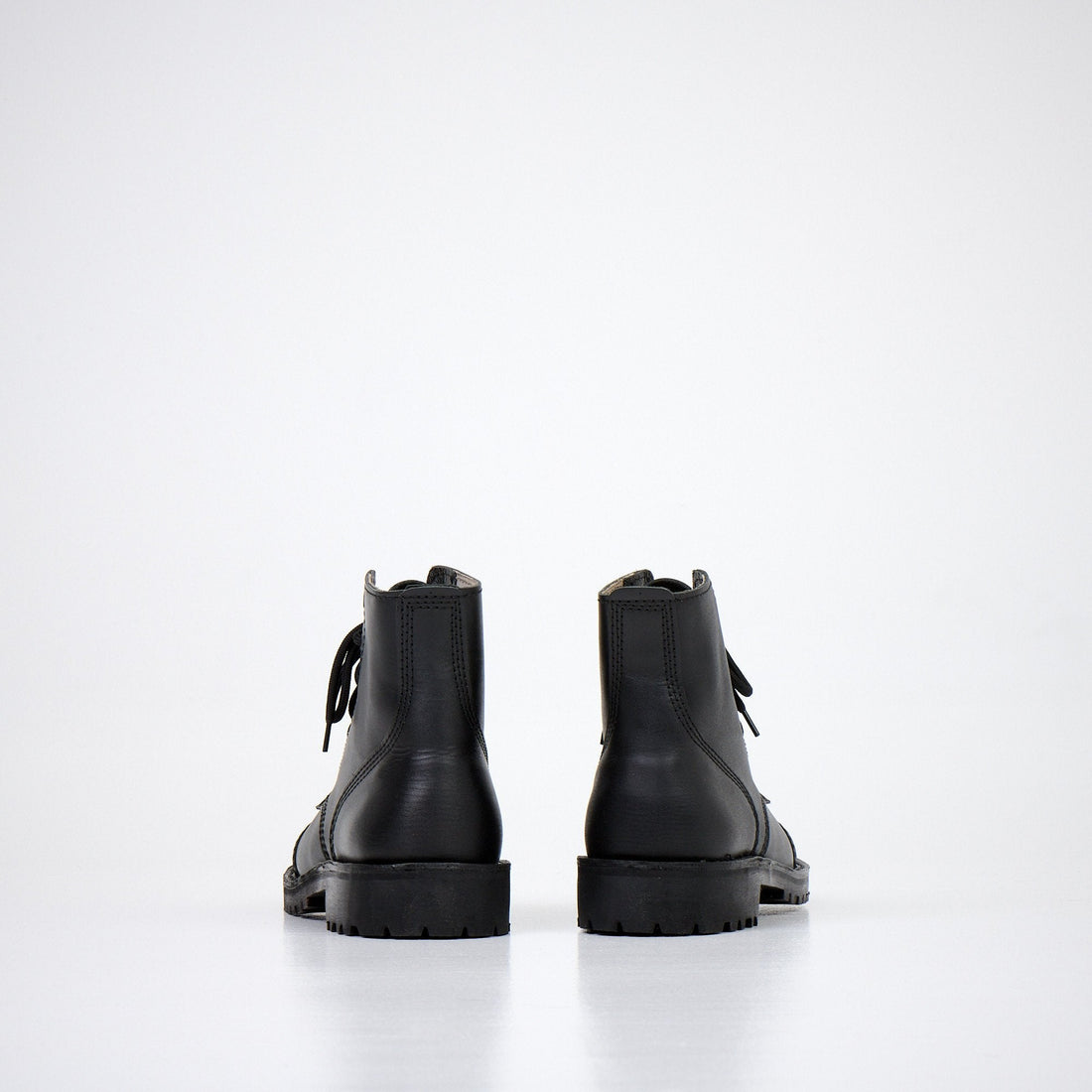 1. Back view of AIPI A-PS-2 black leather boots with lace-up closure, showcasing durable rubber sole in studio setting