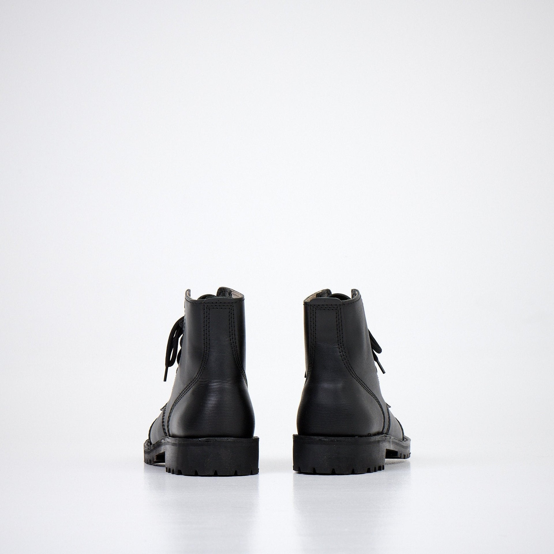 1. Back view of AIPI A-PS-2 black leather boots with lace-up closure, showcasing durable rubber sole in studio setting