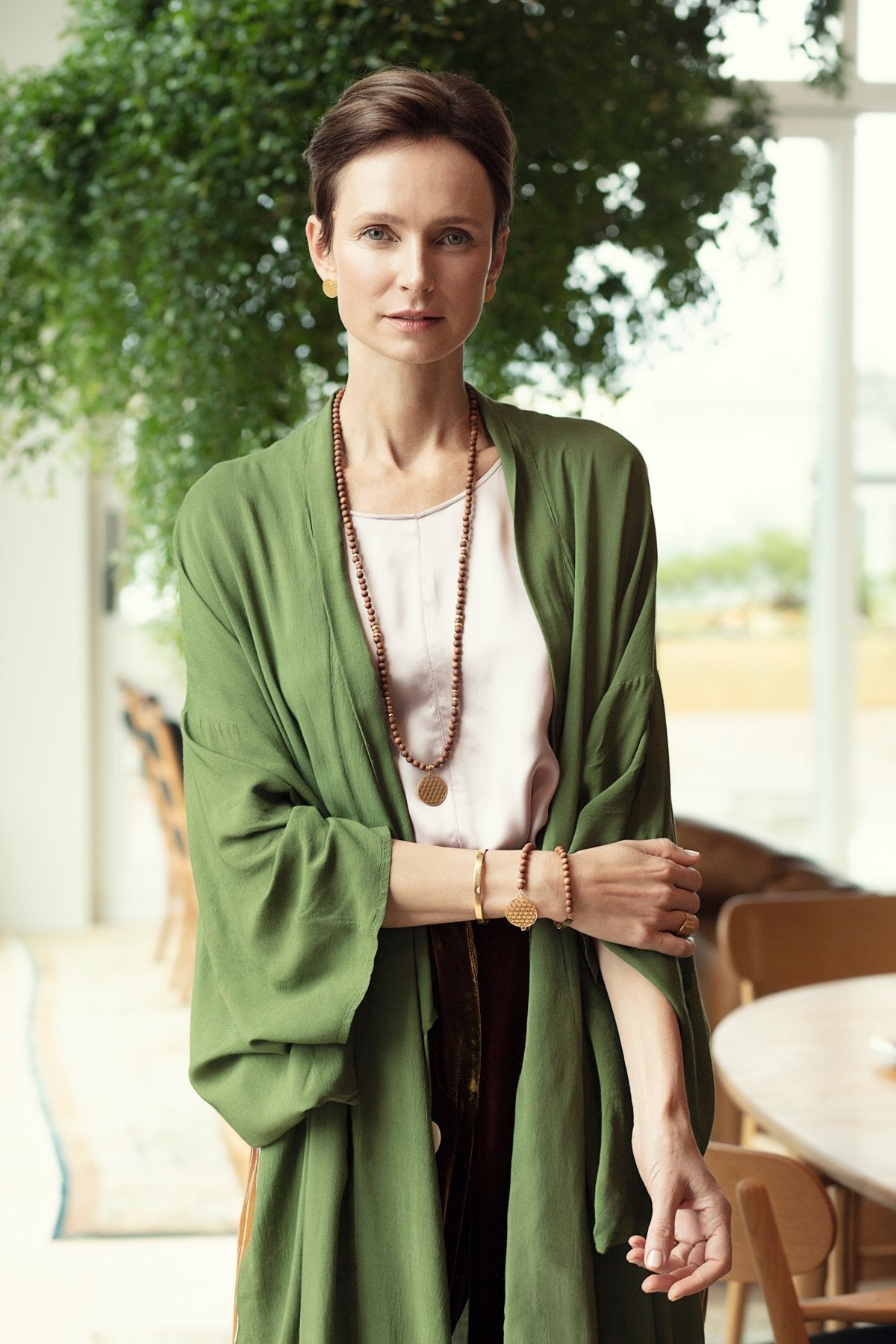 1. Woman wearing New Vintage by Kriss Flower Of Life Bracelet in sandalwood and gold, styled with green kimono in lifestyle setting