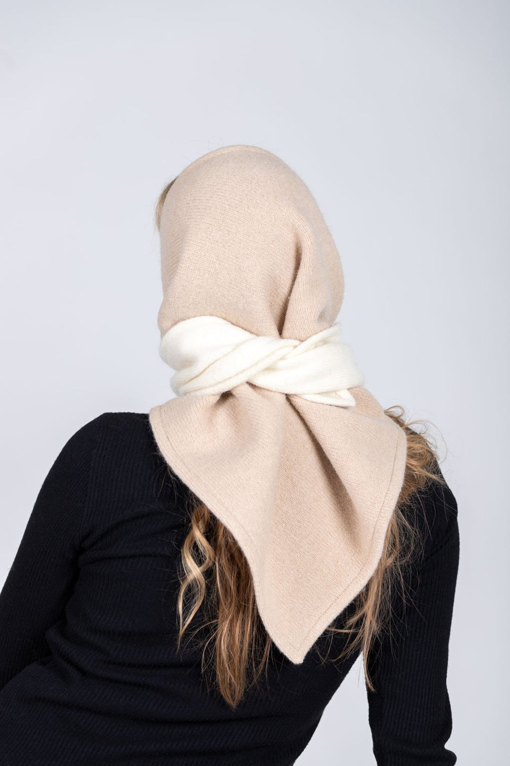 4. Back view of women's HERTTA wool triangle shawl in beige and white, styled as a hood in a studio setting