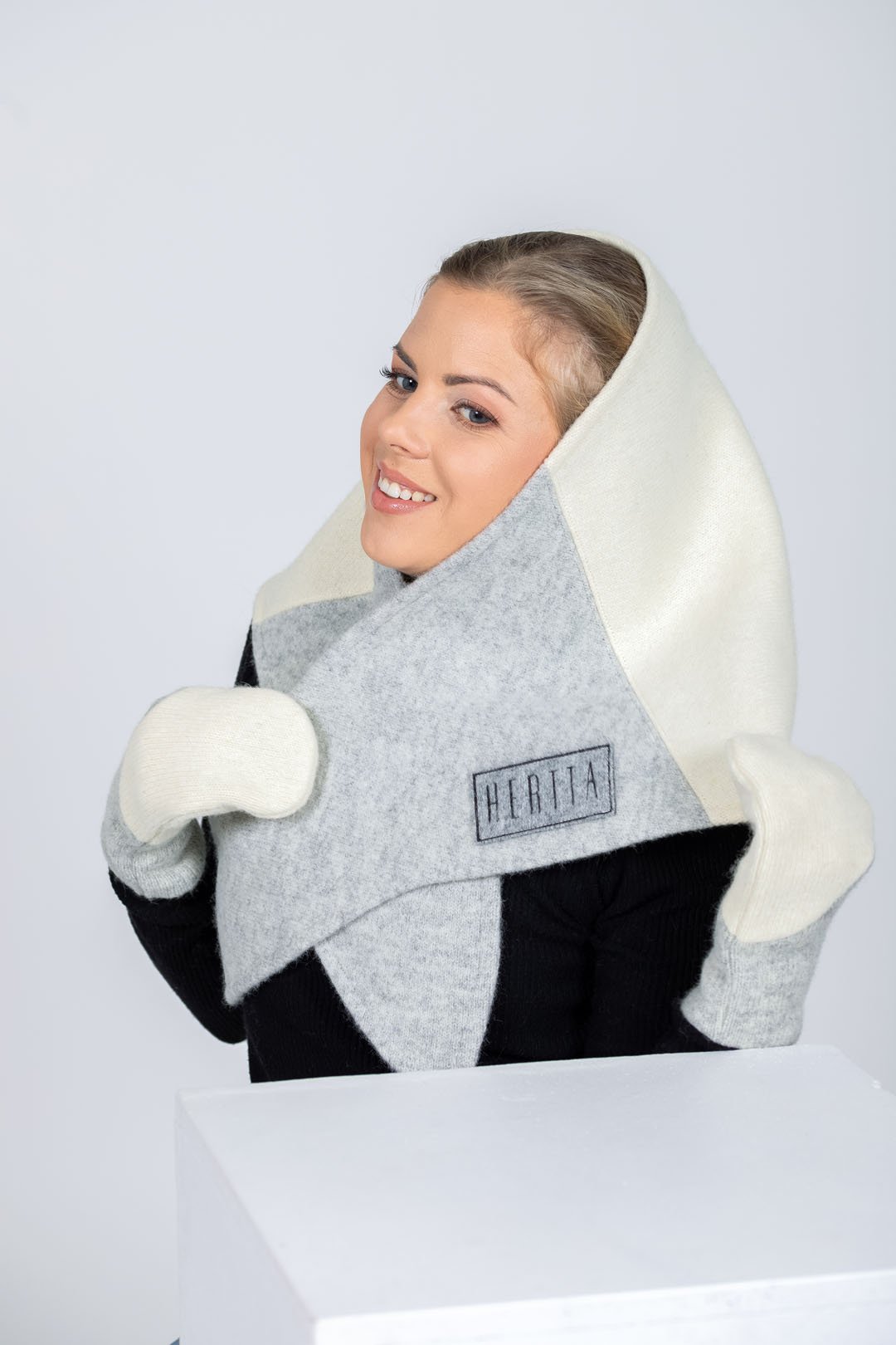 2. Women's HERTTA wool triangle shawl in white and lightest grey, worn as a hood with embroidered logo, studio shot
