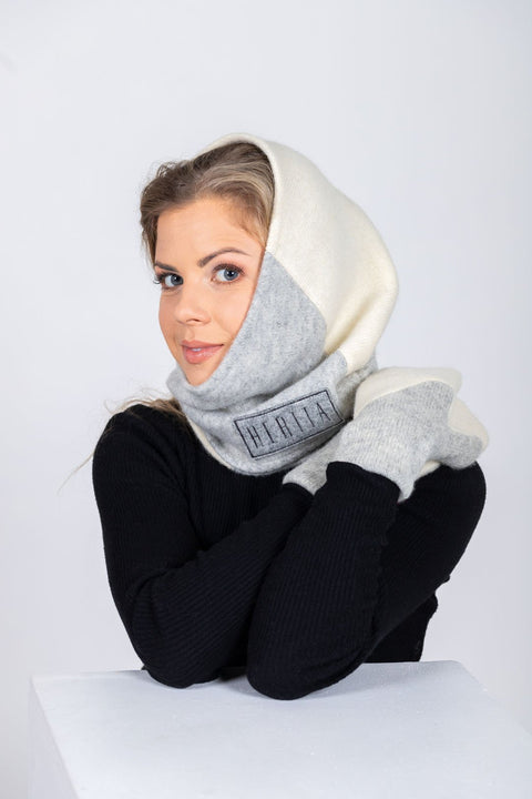 3. Close-up of women's HERTTA wool triangle shawl in white and lightest grey, styled as a hood, showing embroidered logo