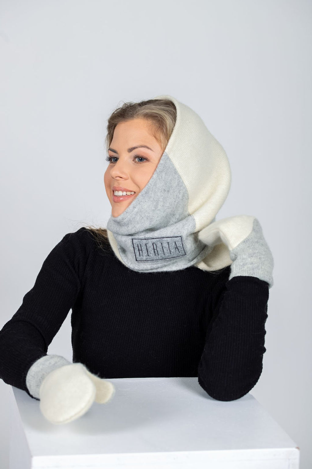 1. Women's versatile handmade wool triangle shawl in white and lightest grey by HERTTA, styled as a hood in studio setting