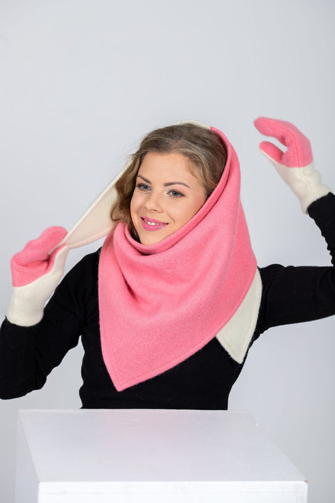 4. Woman adjusting HERTTA pink and white wool triangle shawl worn as a hood with matching mittens, studio setting