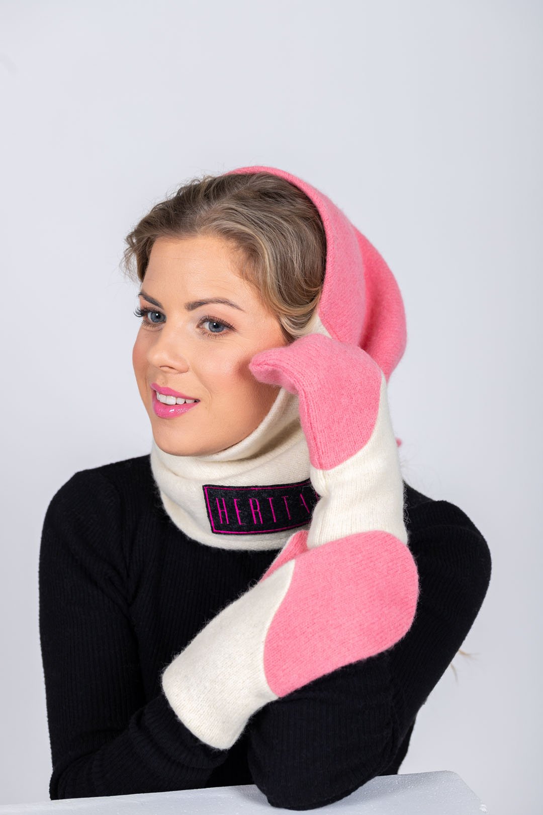 1. Woman wearing HERTTA pink and white wool triangle shawl as a hood with matching mittens, studio setting