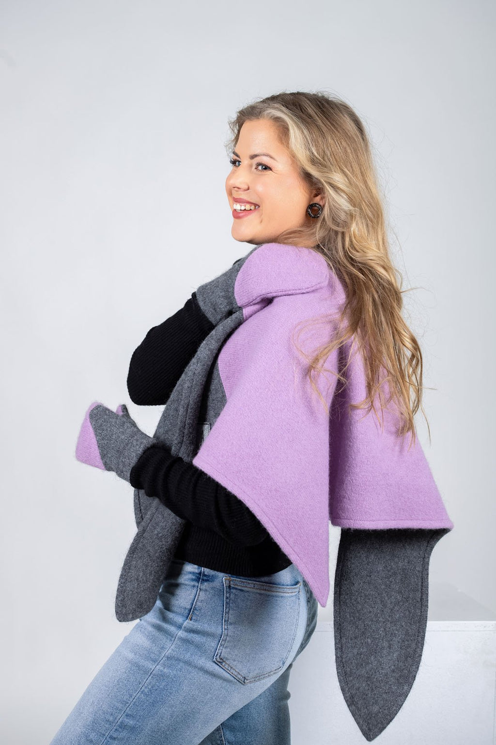 3. Woman draping HERTTA lilac and medium grey wool triangle shawl over shoulders, shown from side in studio