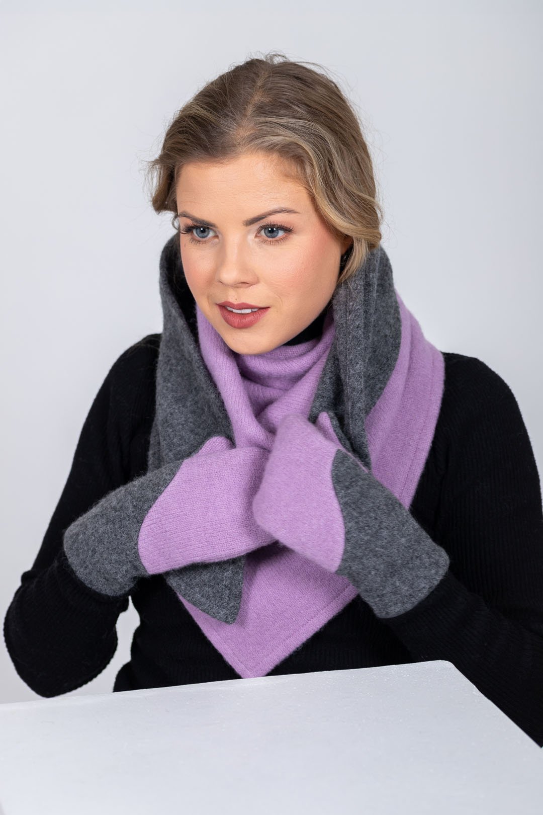 4. Woman wrapping HERTTA lilac and medium grey wool triangle shawl around neck with matching mittens in studio