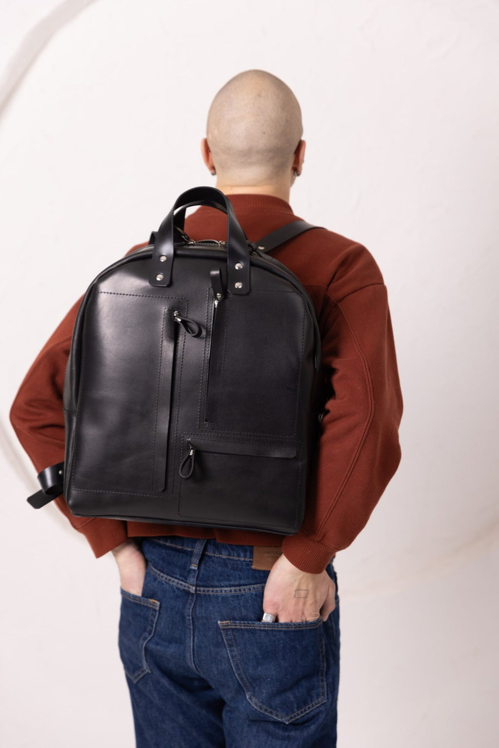 6. Man wearing TOKS VISOKS GORDON black leather backpack, shown from back in studio setting