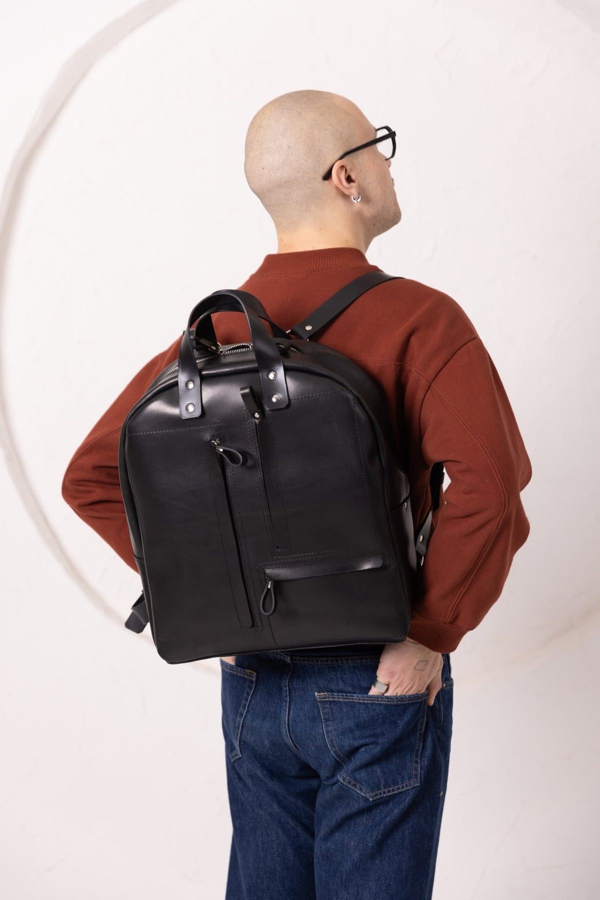 14. Man wearing TOKS VISOKS GORDON black leather backpack, shown from back in studio setting