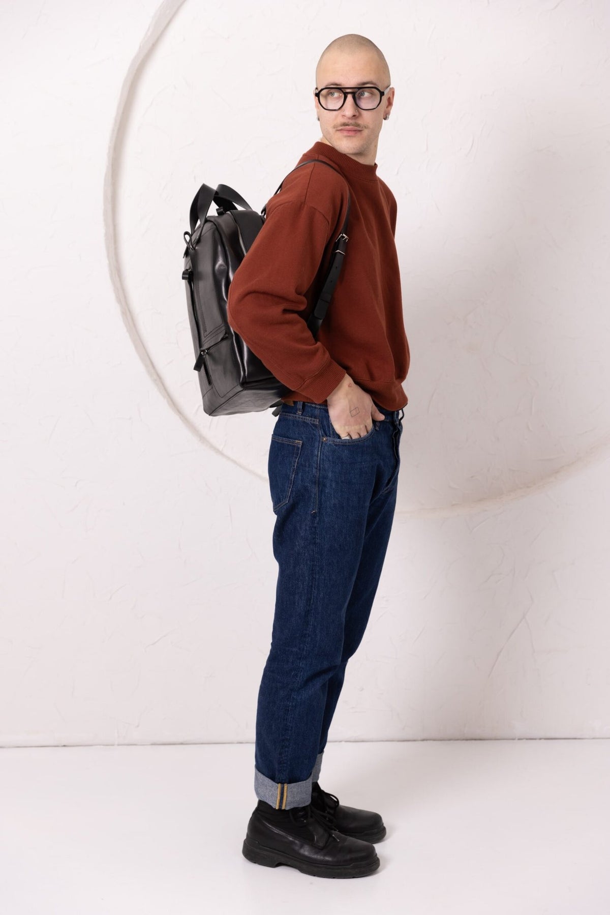 9. Man wearing TOKS VISOKS GORDON black leather backpack, shown from side in studio setting