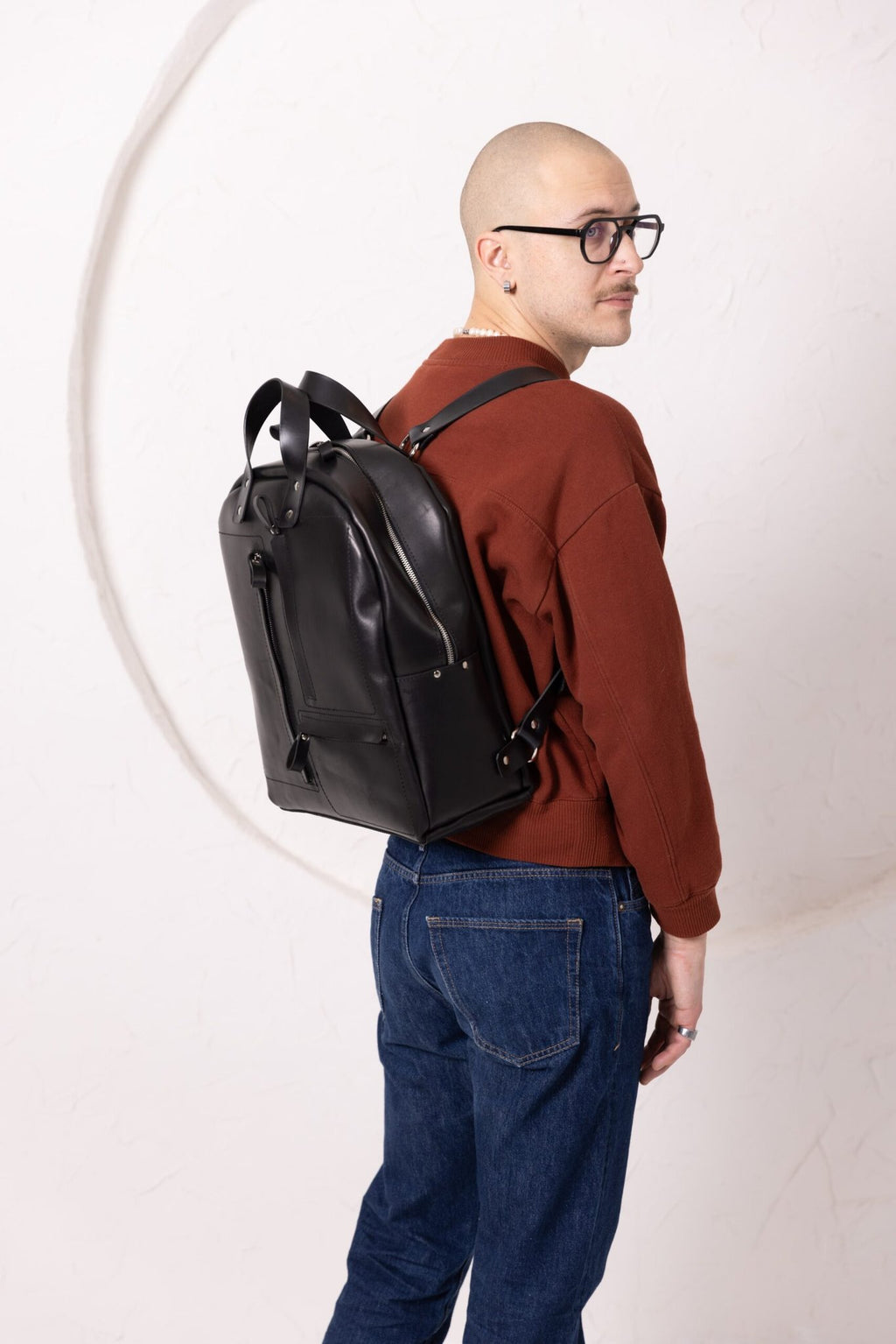 10. Man wearing TOKS VISOKS GORDON black leather backpack, shown from back in studio setting