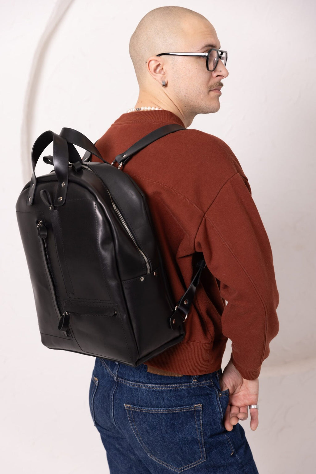 11. Man wearing TOKS VISOKS GORDON black leather backpack, highlighting sleek design in studio setting