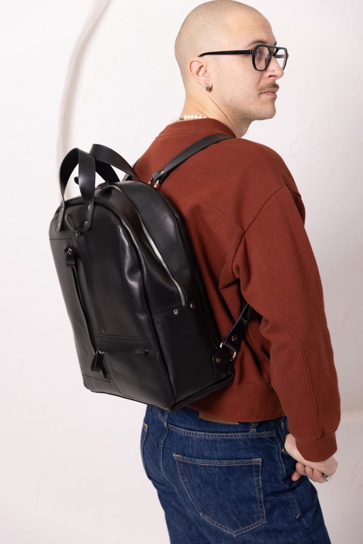 12. Man wearing TOKS VISOKS GORDON black leather backpack, showcasing adjustable straps in studio setting