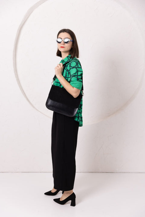 2. Woman wearing TOKS VISOKS ASTORIA black suede handbag crossbody, styled with green top and black pants, in studio setting