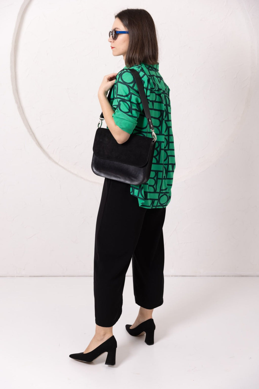 5. Woman in studio wearing TOKS VISOKS ASTORIA black suede handbag, styled with green top and black pants