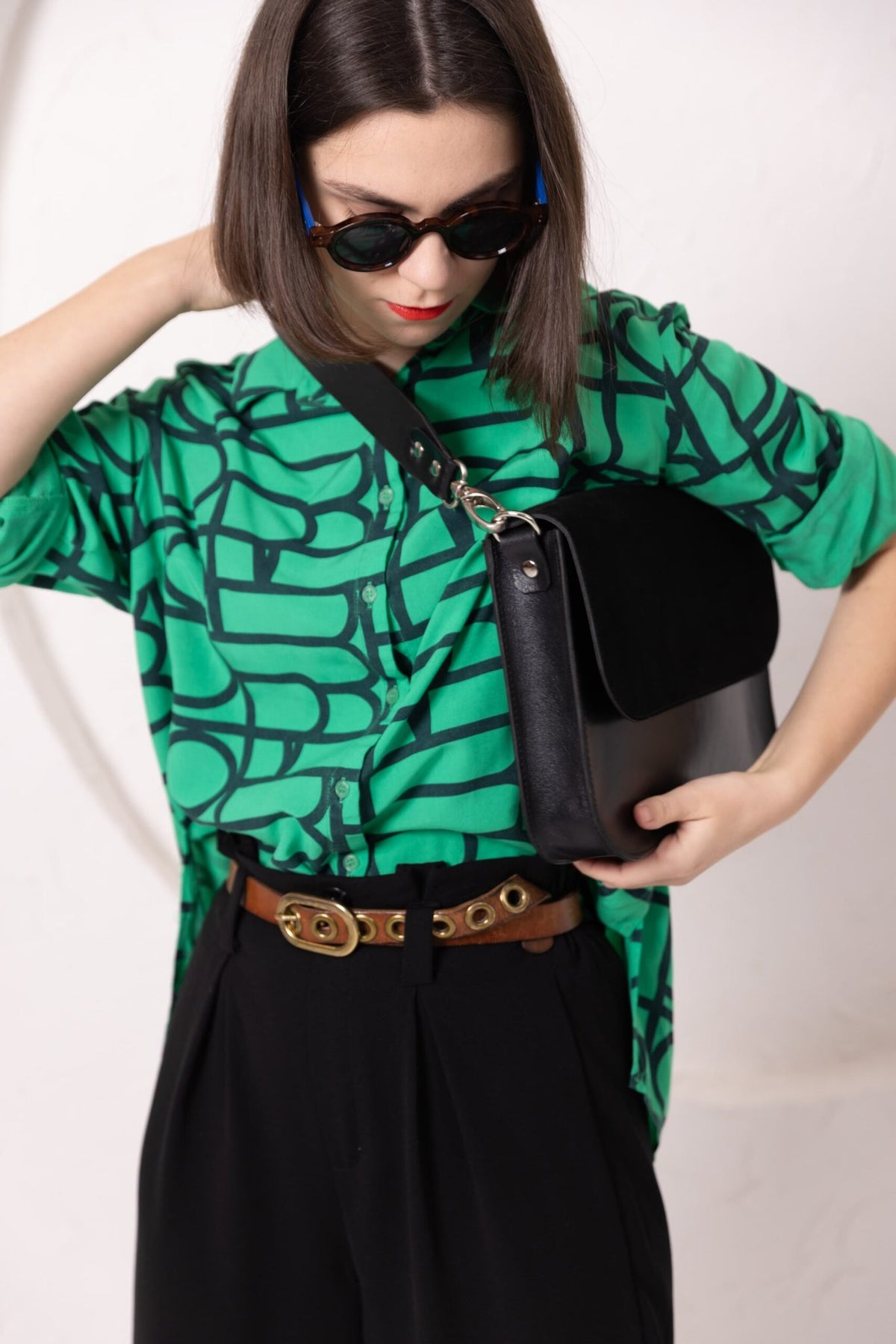 7. Close-up of woman adjusting TOKS VISOKS ASTORIA black suede handbag, styled with green top