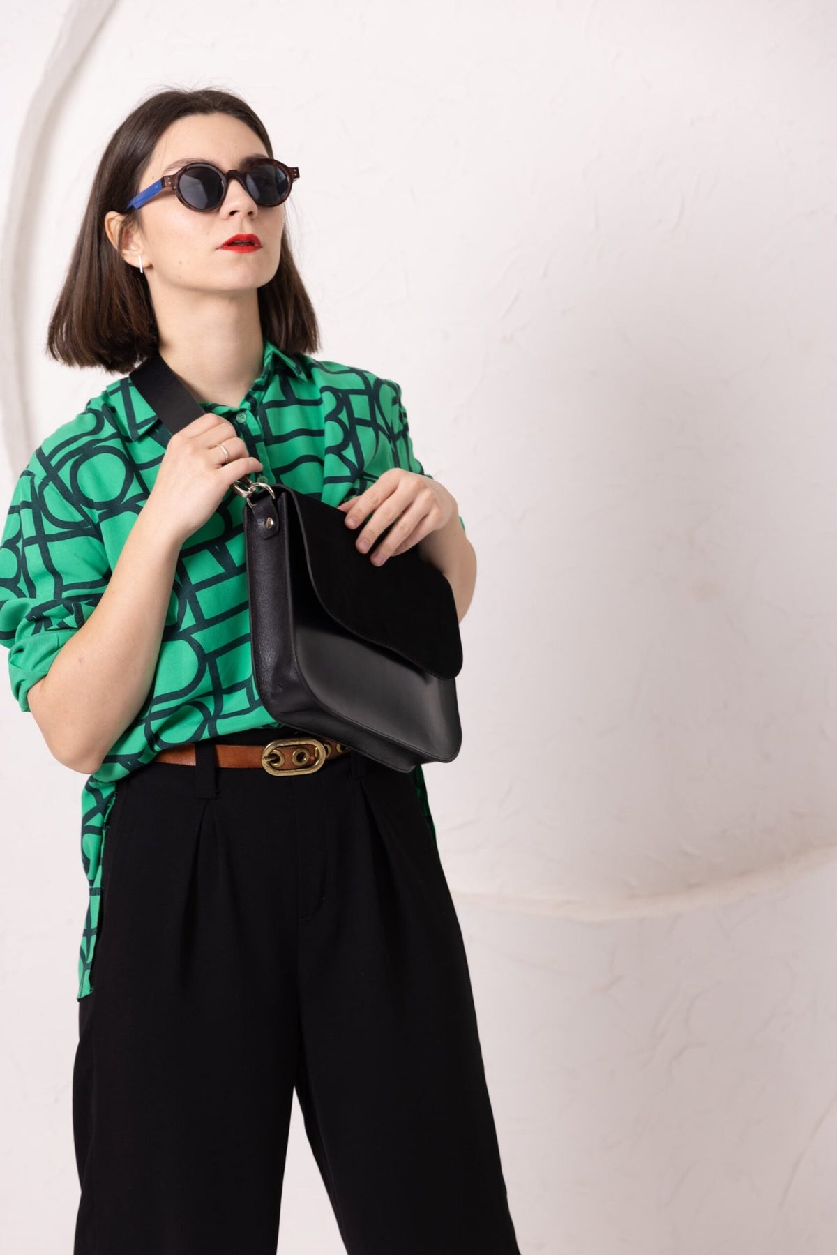 8. Woman holding TOKS VISOKS ASTORIA black suede handbag, styled with green top and sunglasses