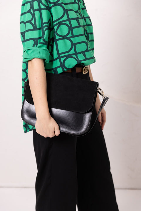 1. Woman holding TOKS VISOKS ASTORIA black suede handbag with short shoulder strap, styled with green patterned top and black pants