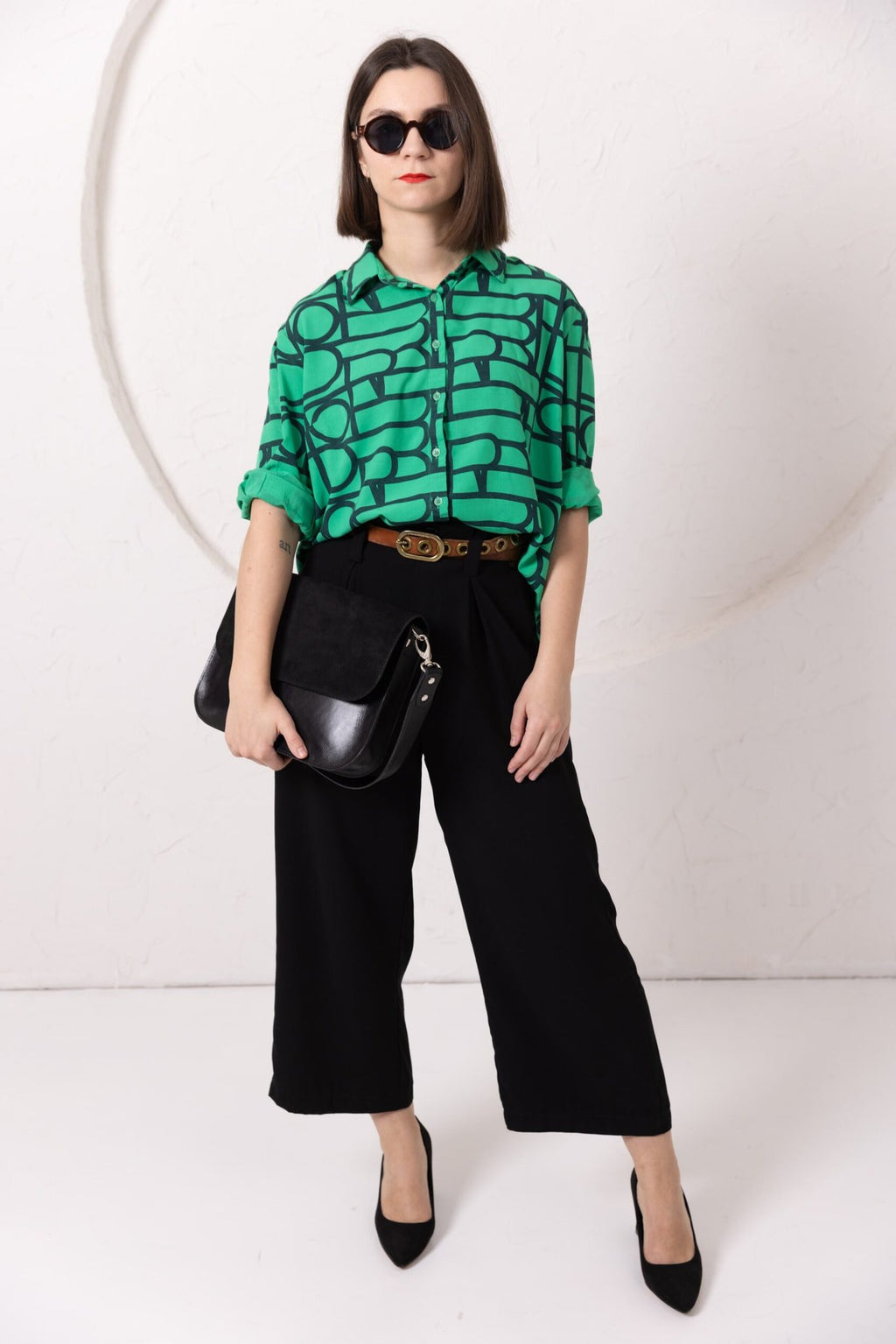 9. Woman posing with TOKS VISOKS ASTORIA black suede handbag, styled with green top and black pants