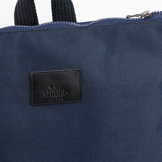 6. Detailed view of Muni logo on navy blue backpack with leather bottom