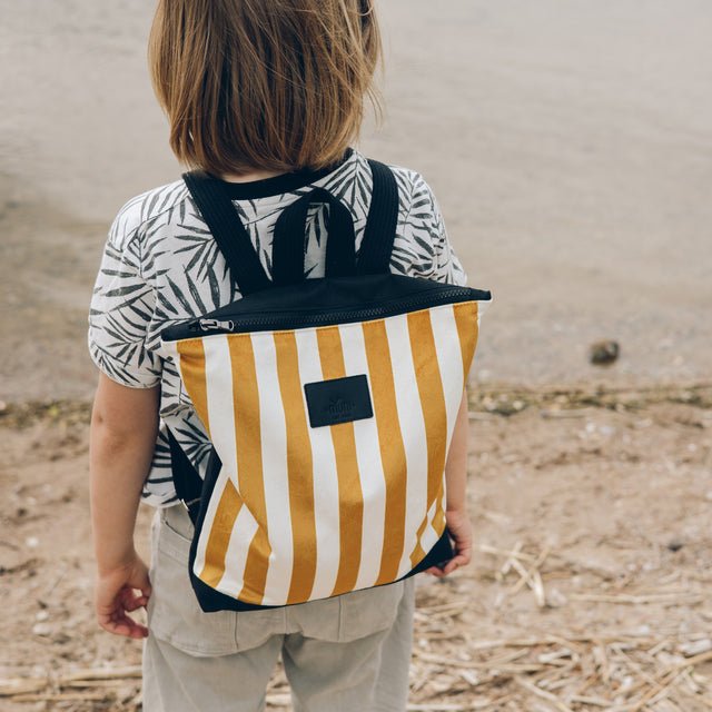 2. Child wearing Muni striped mustard and white backpack on a sandy path