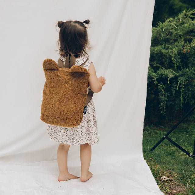 1. Child wearing Muni brown teddy backpack in outdoor setting, showing adjustable straps and playful design