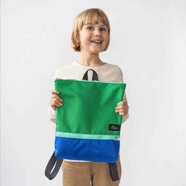 1. Child holding Muni waterproof kids backpack in green and blue, showcasing front design