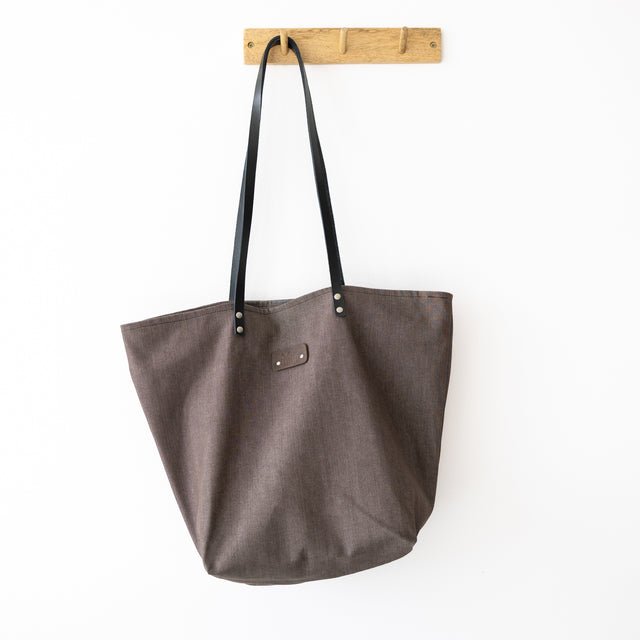 5. Muni brown denim tote bag with black leather handles hanging on a wooden hook in a studio setting