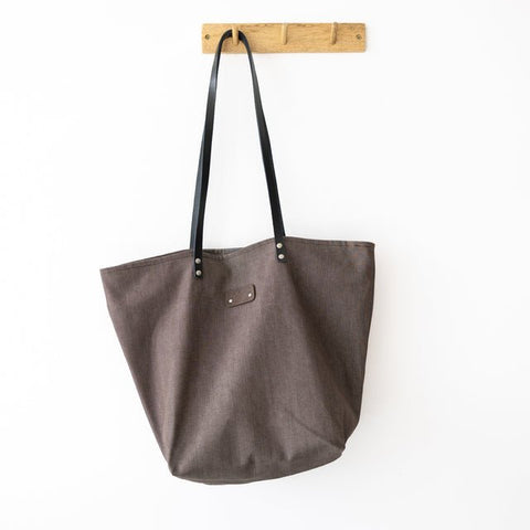 5. Muni brown denim tote bag with black leather handles hanging on a wooden hook in a studio setting