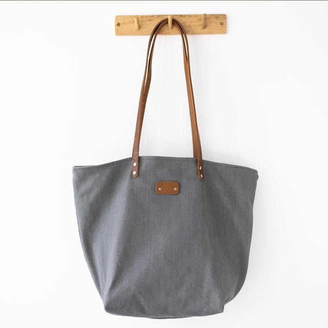 6. Close-up of Muni grey denim tote bag with tan leather handles, showing brand logo and metal rivets