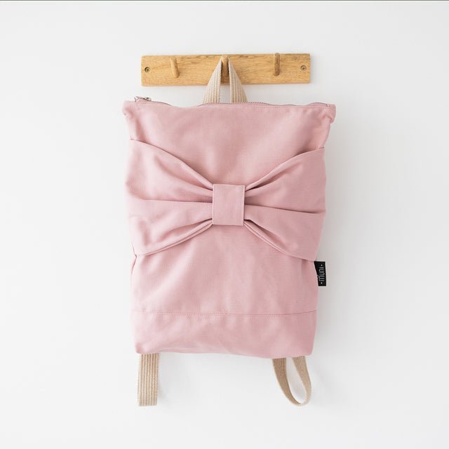 8. Muni Pink Bow backpack hanging on hook, displaying large bow and pink denim