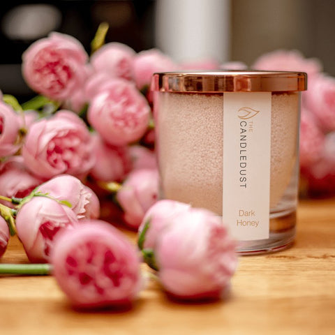 5. Candledust Dark Honey powdered candle in glass with rose gold lid, surrounded by pink flowers