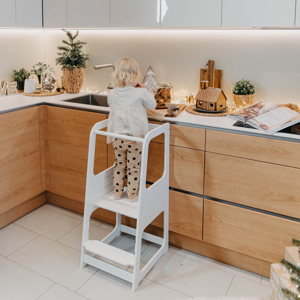 19. Child using white Montessori helper tower step stool in festive kitchen