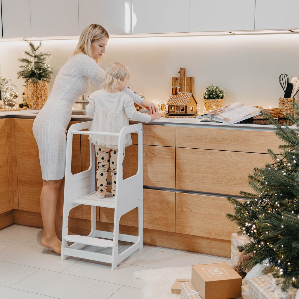 16. Woman and child using white Montessori helper tower step stool in decorated kitchen