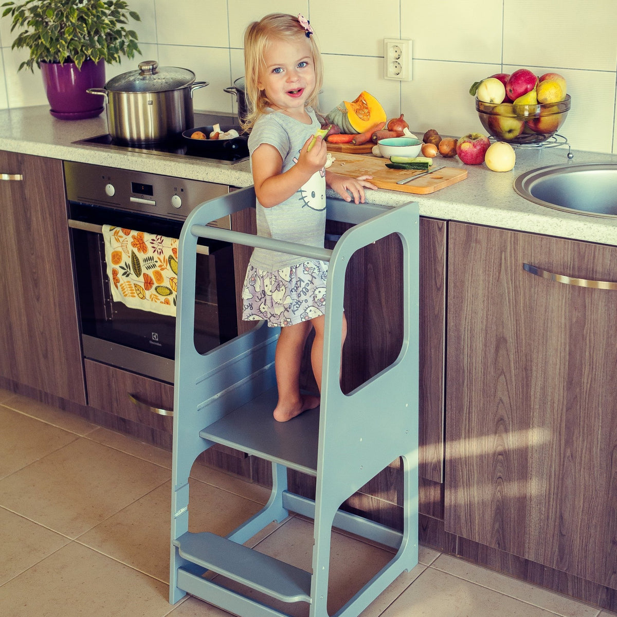 4. Child on blue Montessori helper tower step stool in kitchen with fruit