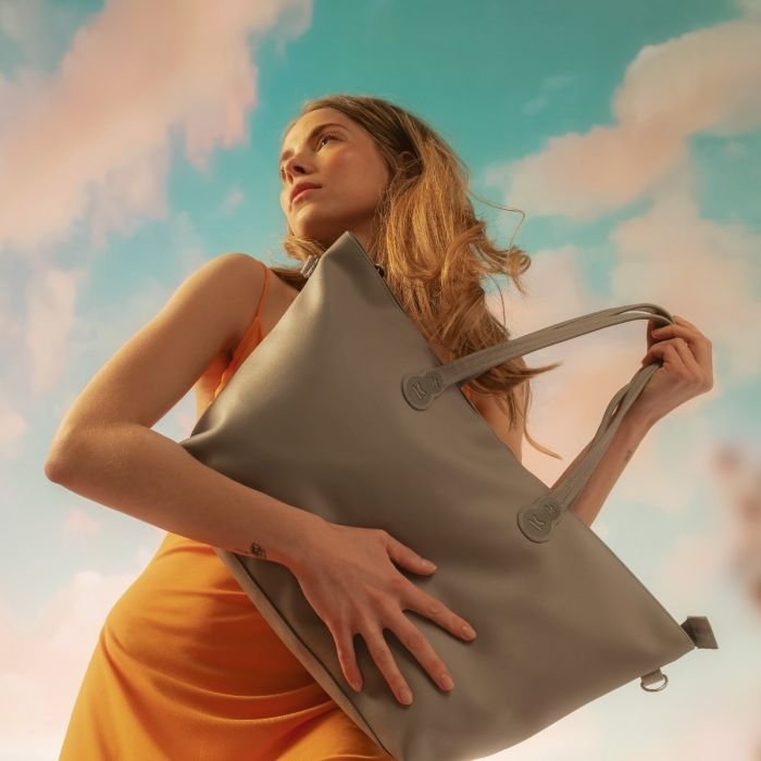 1. Woman holding light grey Kinderkraft Treasurebag against a sky background