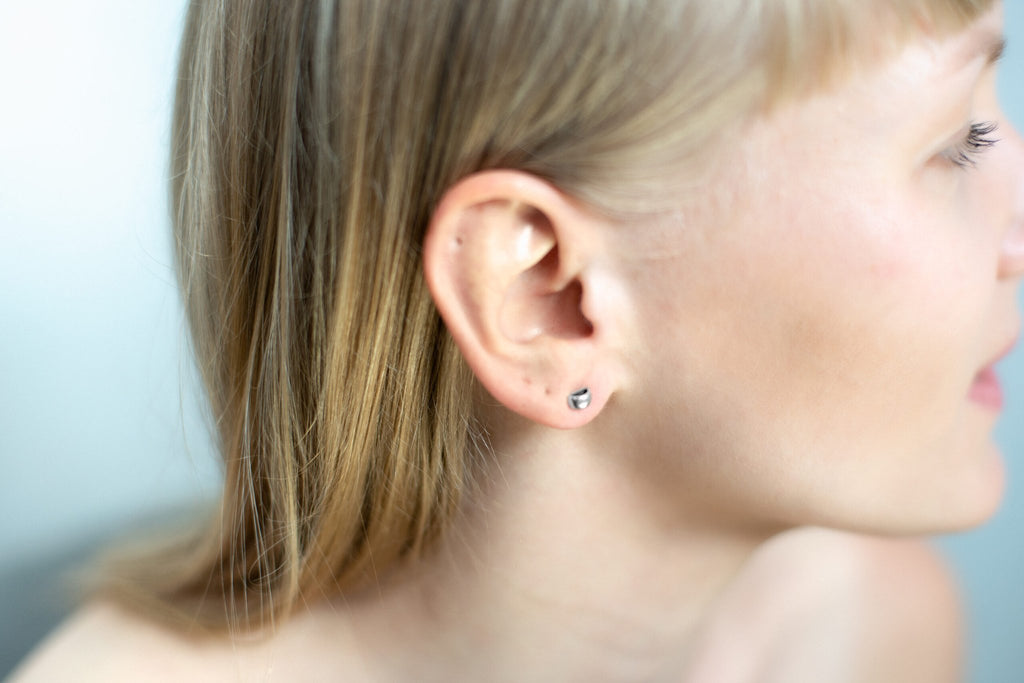 1. Woman wearing Maarja Palu HOLLOW small stud earrings in polished silver, showcasing minimalist half-circle design