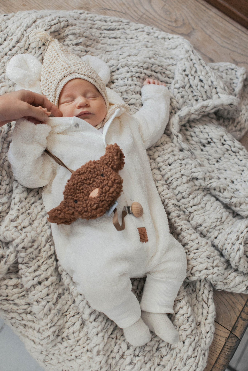 3. Baby lying on knitted blanket in fuzzy ecru jumpsuit with bear ears hood and knit hat