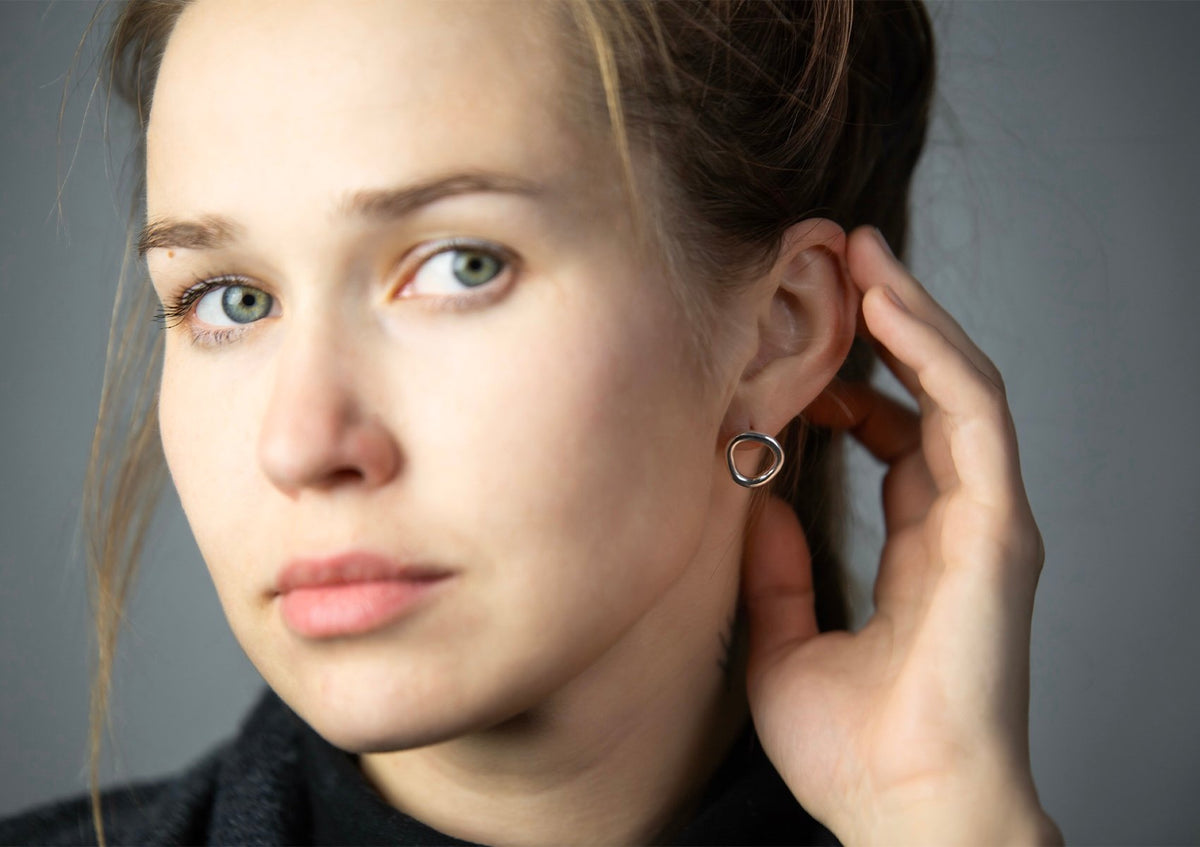 1. Woman wearing Maarja Palu Earrings IRREGULAR x1 in polished silver, showcasing asymmetrical circular design
