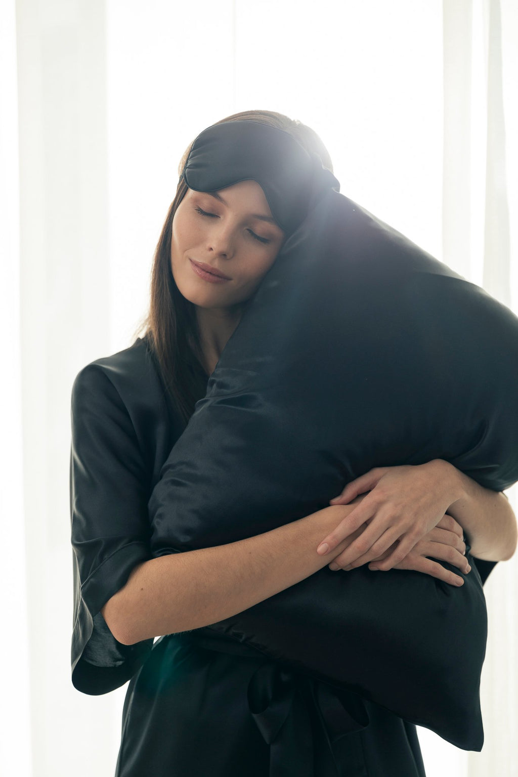 1. Woman holding black Mulberry silk pillowcase in bright room, showcasing luxurious texture