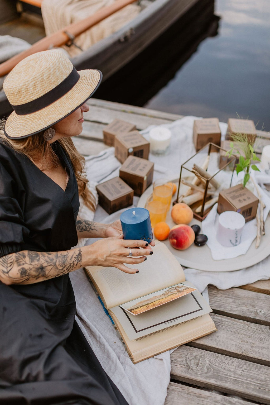 1. Woman enjoying a picnic by the water with TL Candles hand-made blue soy wax candle, surrounded by fruits and books