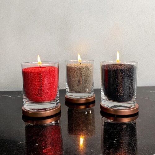 4. Trio of Candledust powder candles in red, beige, and black, burning in glass containers on a black surface